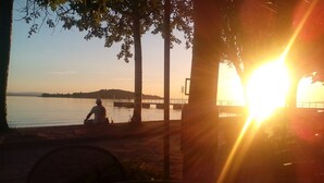 Iemand zit aan de oever van een meer bij zonsondergang, met een brug op de achtergrond.