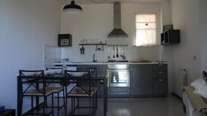 Een kleine keuken met een eethoek, met een fornuis, oven en hangende keukengerei.