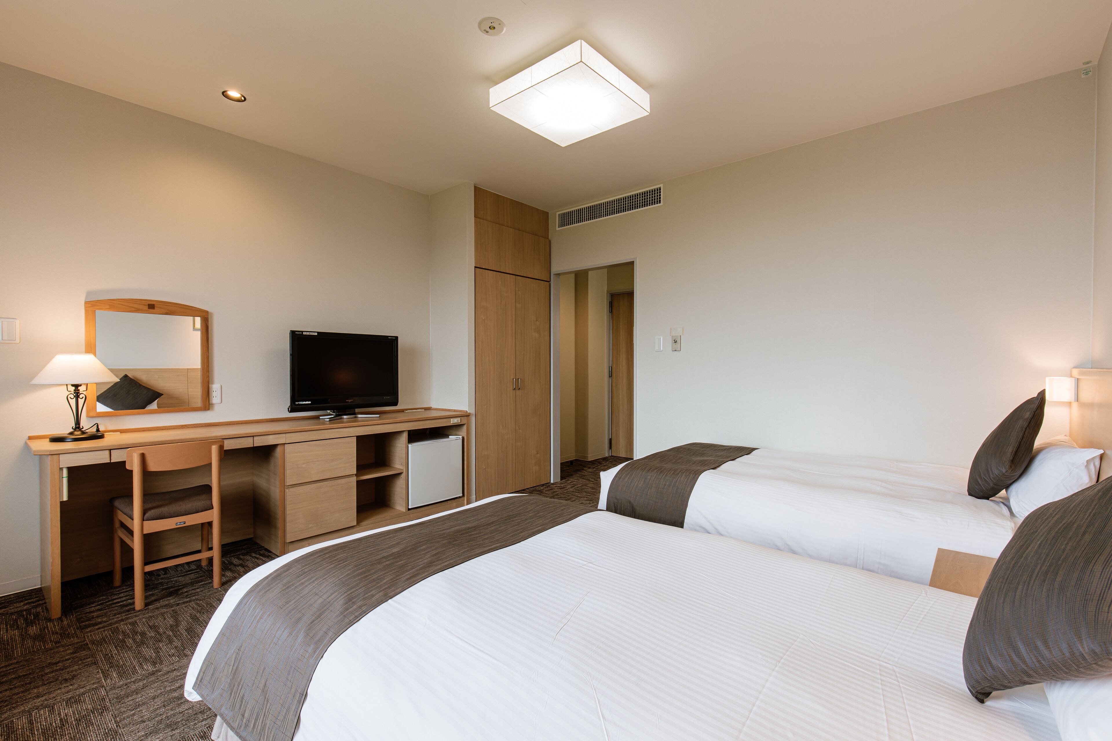 A hotel room with two beds, a desk, a television, and a mirror.