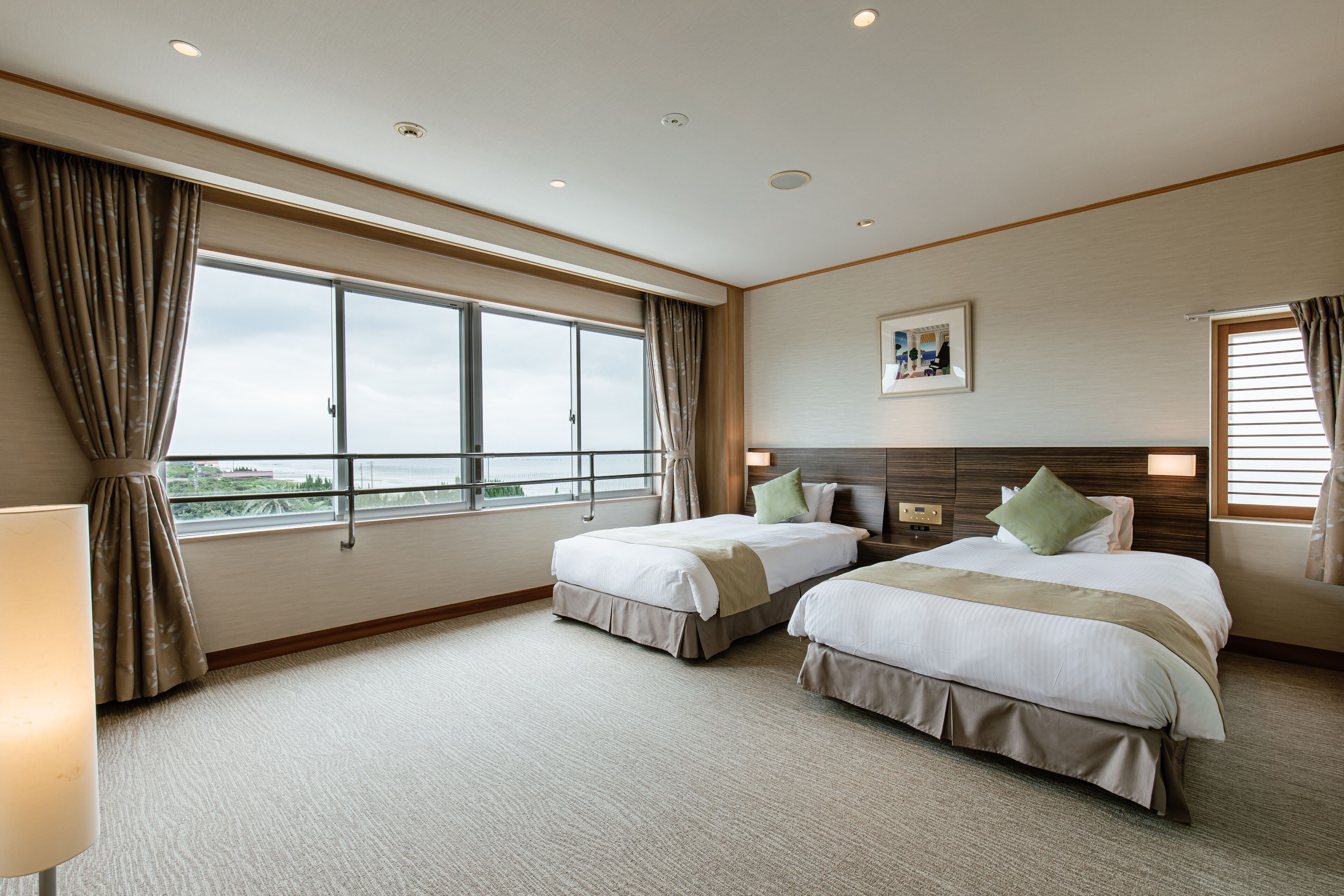 A hotel room with two beds, a large window, and a view of the outdoors.