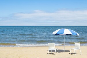 Una playa con dos sillas blancas y una sombrilla azul y blanca.