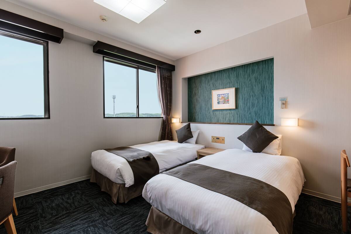 A hotel room with two beds, a desk, and a chair.