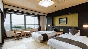 A hotel room with two beds, a desk, and a chair. There is a large window providing a view of the outdoors.