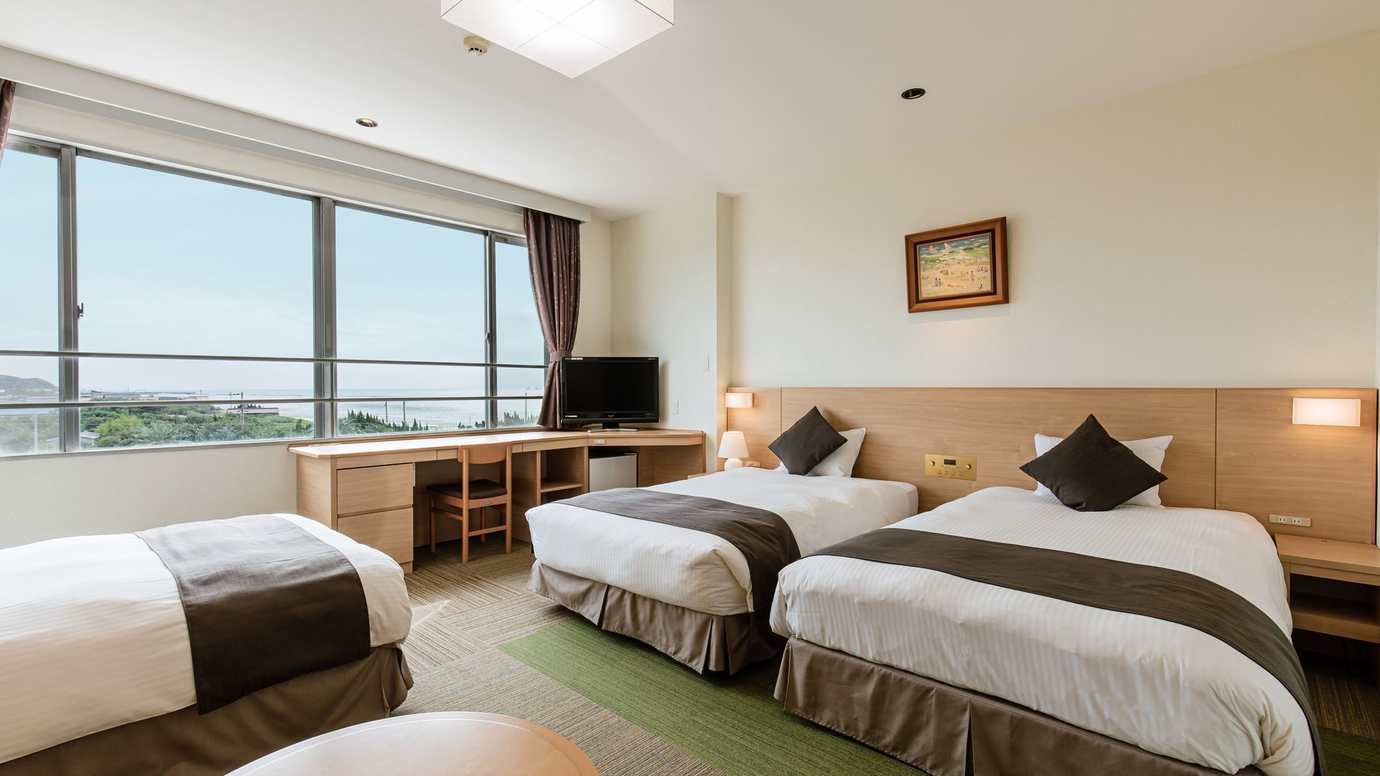 A hotel room with two beds, a desk, a TV, and a large window with a view.
