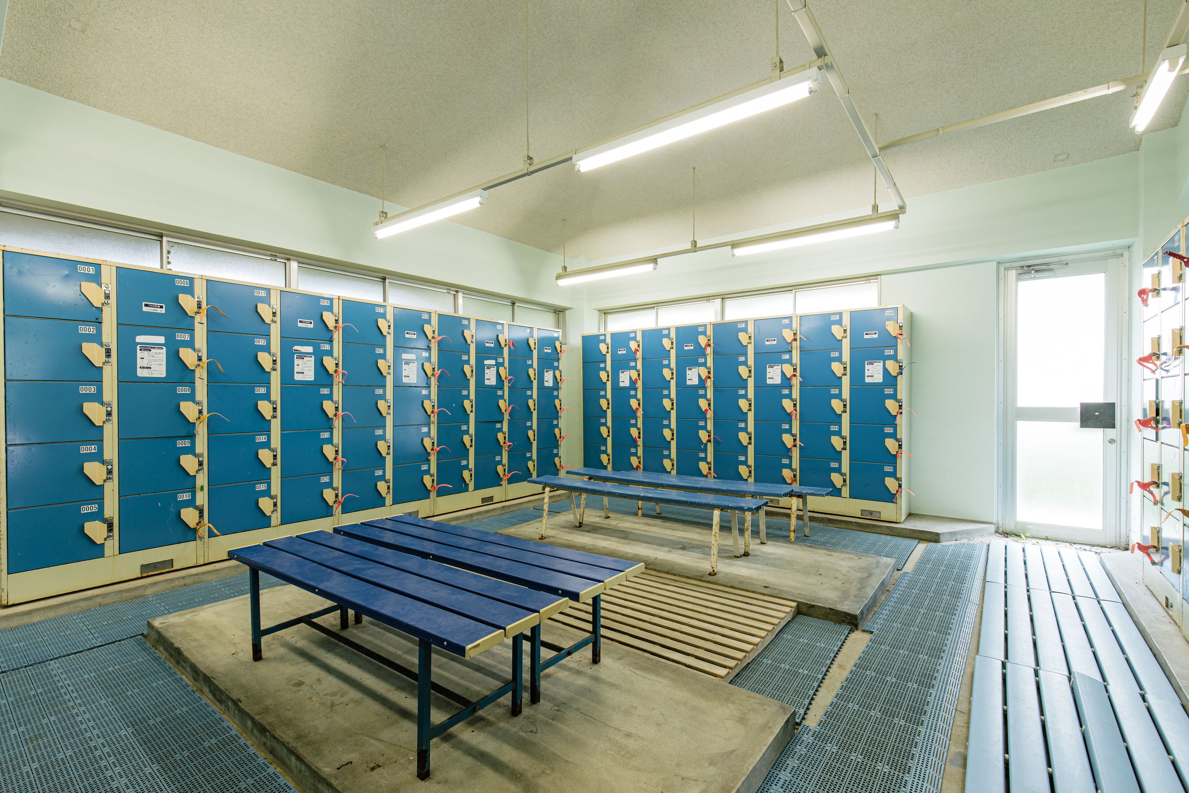 A locker room with multiple blue lockers, benches, and a tiled floor.