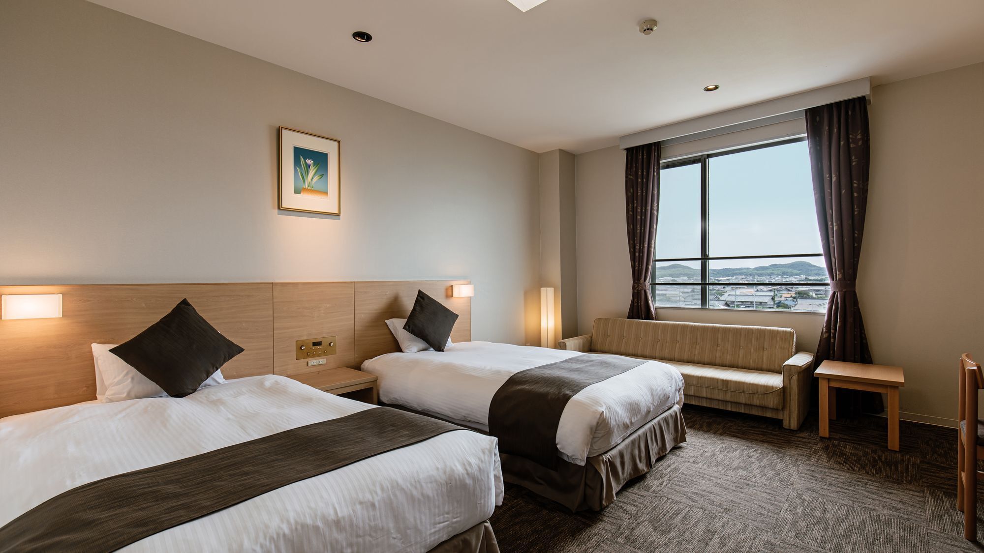 A hotel room with two beds, a sofa, a desk, and a large window with a view.