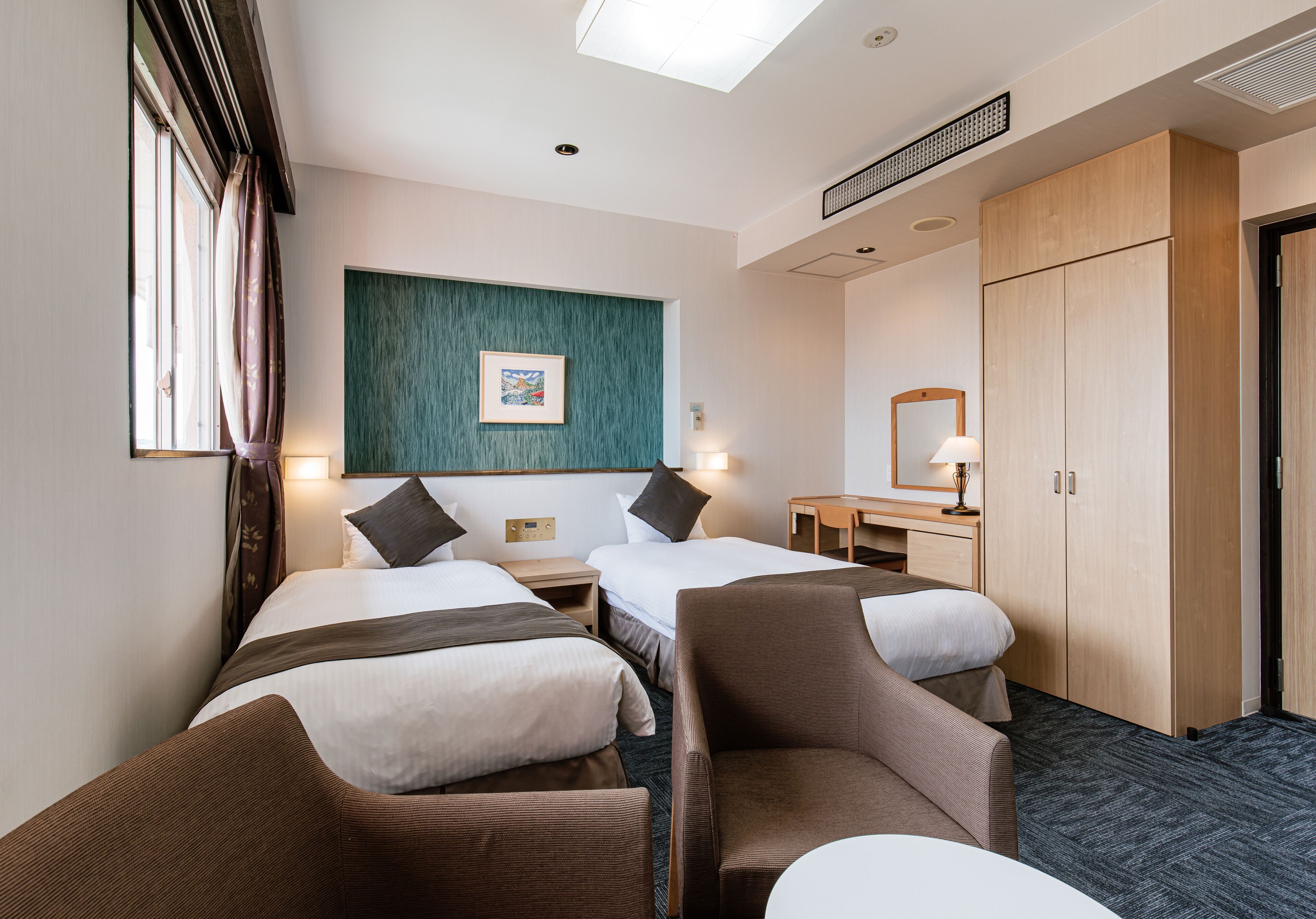 A hotel room with two beds, a desk, a chair, a wardrobe, and a window with curtains.