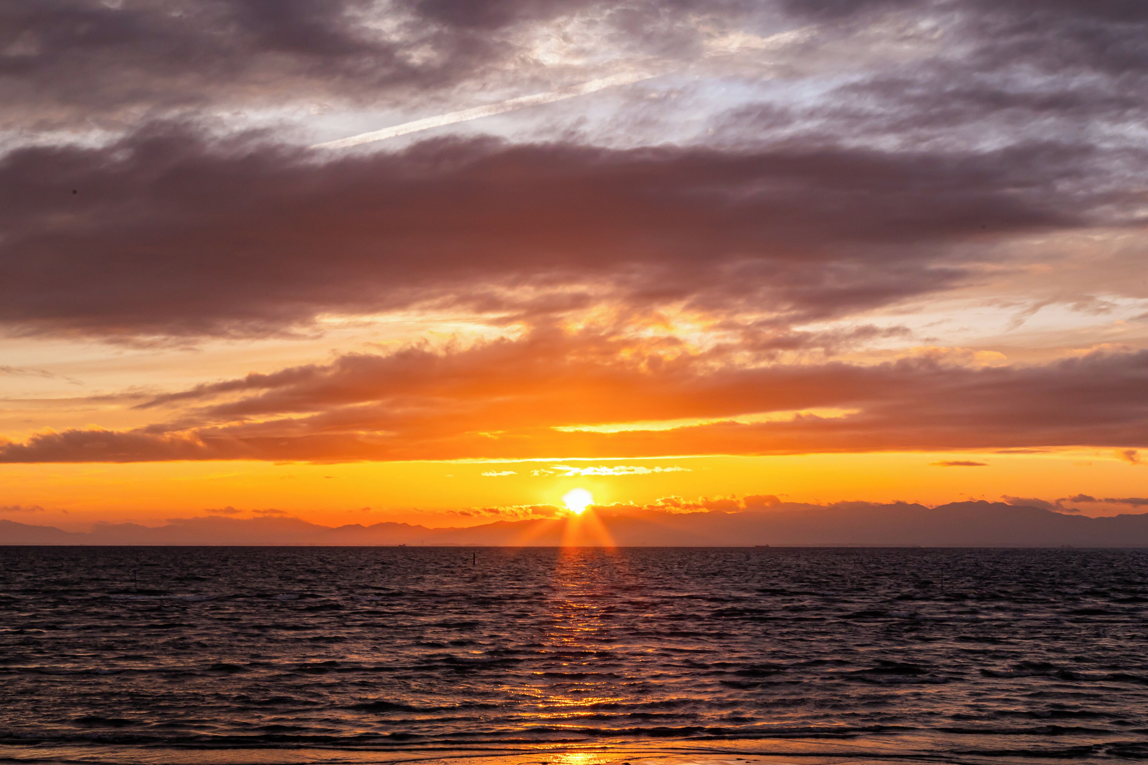Un coucher de soleil sur l’océan, avec un ciel dégagé et une mer calme.