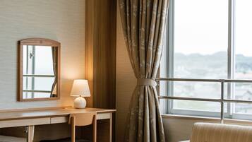 Habitación de hotel con escritorio, silla, lámpara y vistas a través de una ventana con cortinas.
