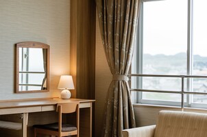 Habitación de hotel con escritorio, silla, lámpara y vistas a través de una ventana con cortinas.