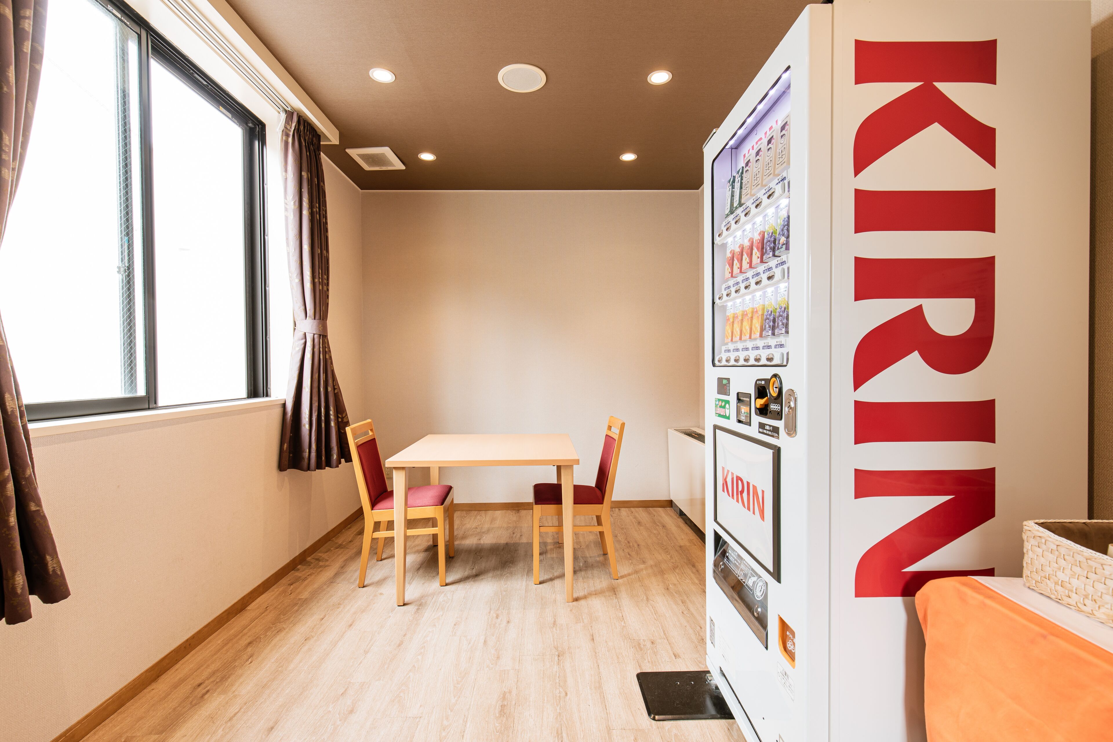 A room with a wooden table and chairs, a vending machine, and a window with curtains.