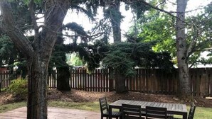 Um deck de madeira com mesa e cadeiras, cercado por árvores e um portão de madeira.