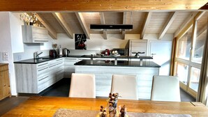 Een moderne keuken met houten balken, een centraal kookeiland en een eethoek met een gedekte tafel voor twee.