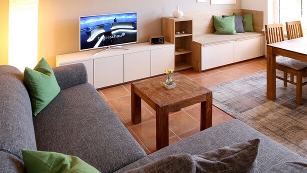 A modern living room with a sofa, coffee table, TV, and a dining area with chairs and a table. - comfortable apartment f. 3 pers., Central, modern furnishings, WLAN, incl. bed linen (Ostseebad Prerow)