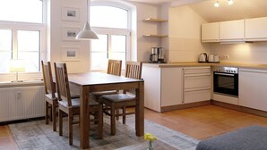 A modern kitchen with white cabinets, a built-in oven, and a dining area with wooden chairs and a table. - comfortable apartment f. 3 pers., Central, modern furnishings, WLAN, incl. bed linen (Ostseebad Prerow)
