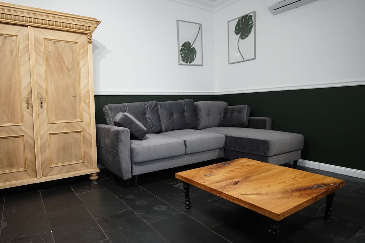 A room with a wooden wardrobe, a grey sofa, and a wooden coffee table.
