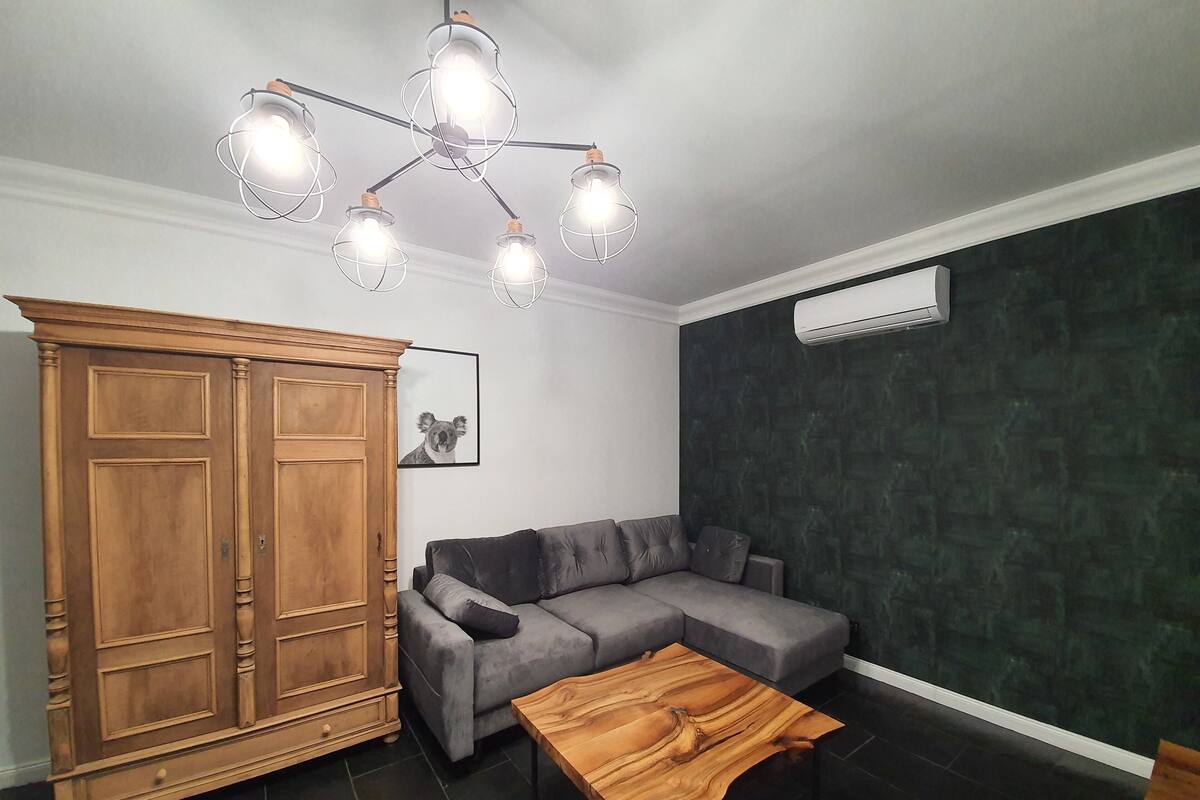 A modern living room with a grey sectional sofa, a wooden cabinet, a wooden coffee table, and a unique ceiling light fixture.