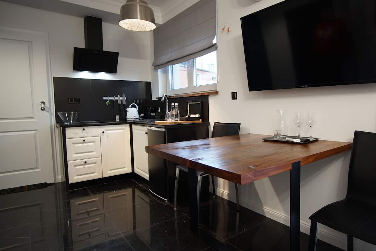 A modern kitchen with a wooden dining table, black chairs, and a flat-screen TV mounted on the wall.