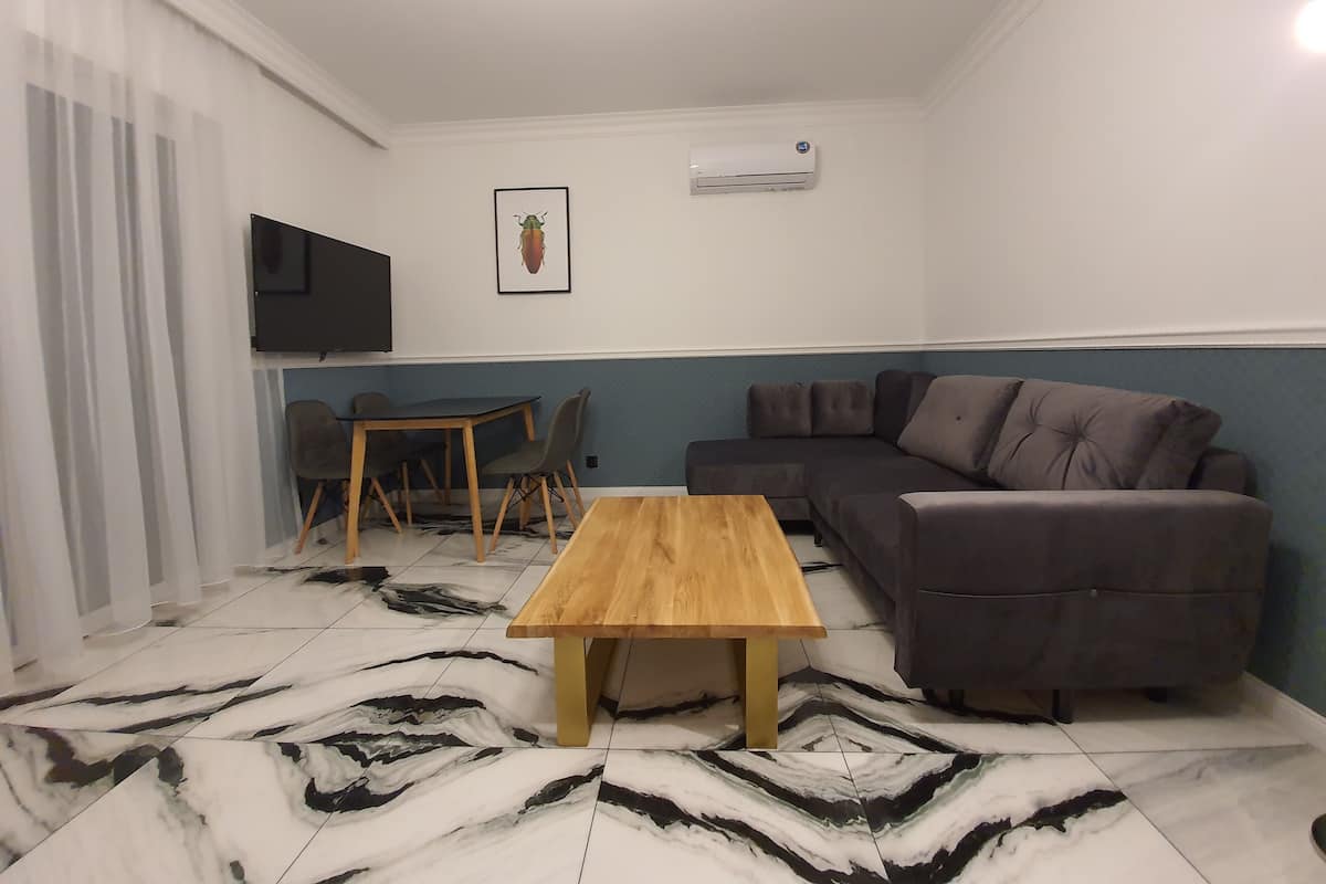 A living room with a wooden coffee table, a grey sofa, a TV mounted on the wall, and a framed picture.
