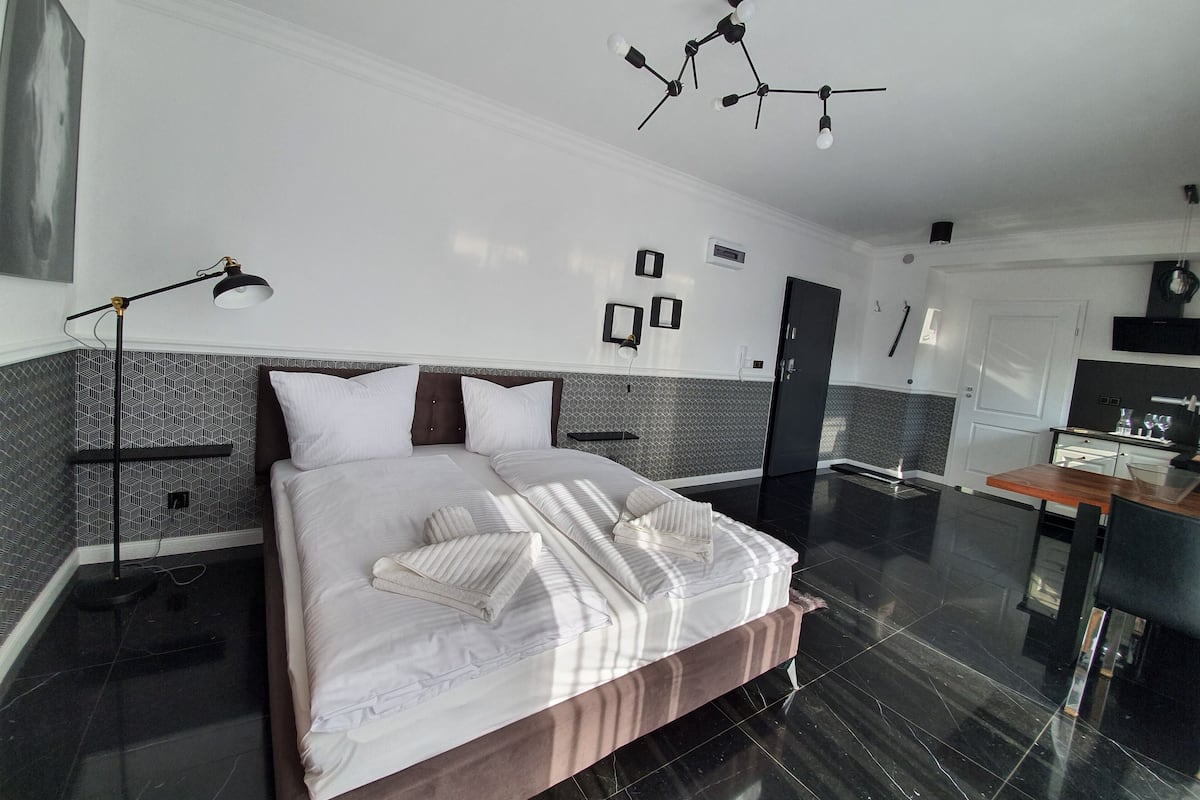A modern hotel room with a large bed, a desk, and a kitchenette.