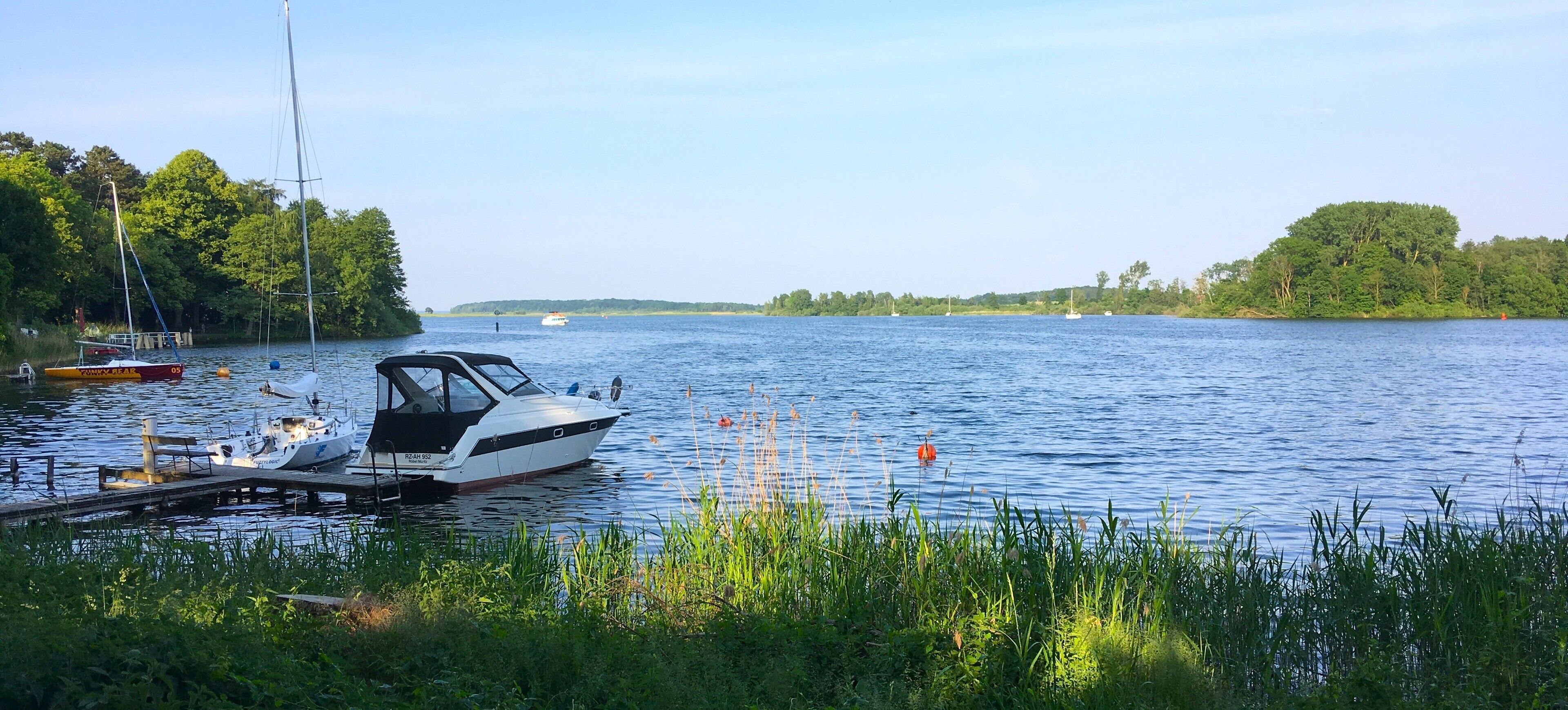 A calm lake with boats docked at a pier, surrounded by lush greenery.