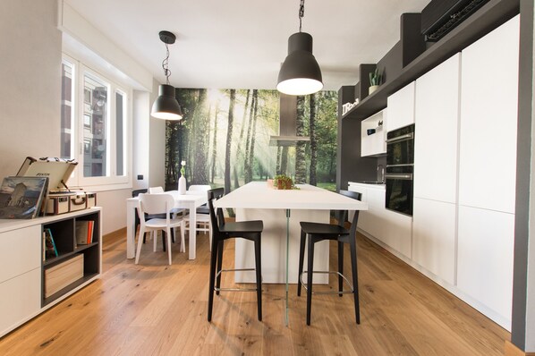 A modern kitchen with a large island, white cabinetry, and black bar stools. - Calìxa (Cagliari)