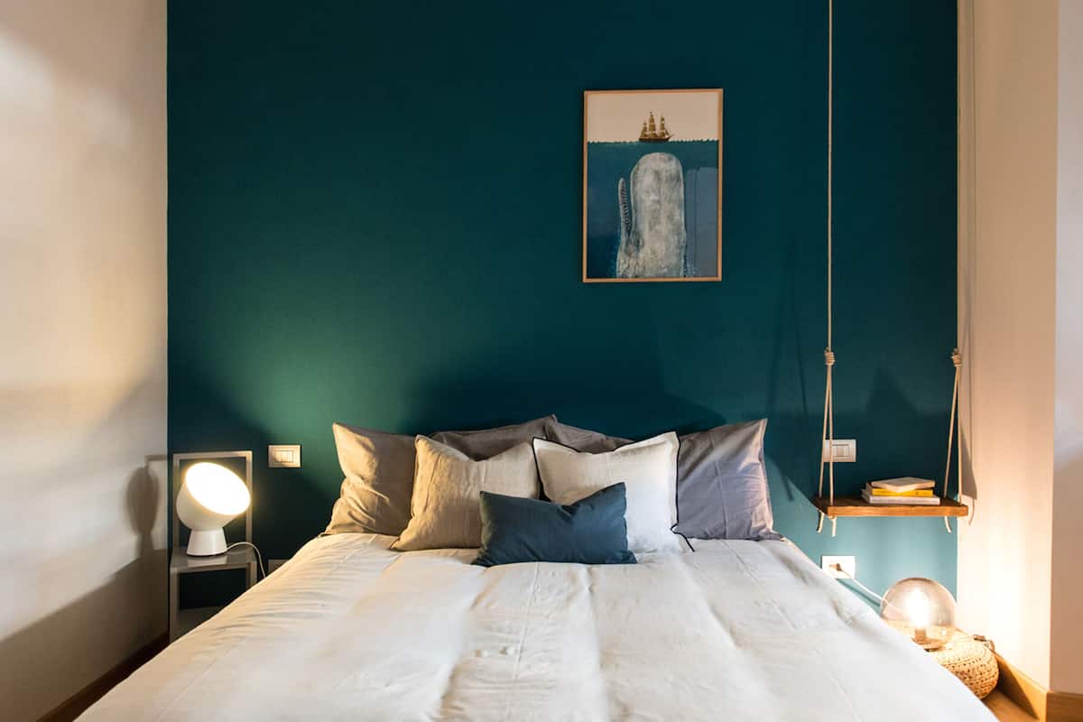 A neatly made bed with pillows, a bedside lamp, and a wall-mounted picture of a ship.
