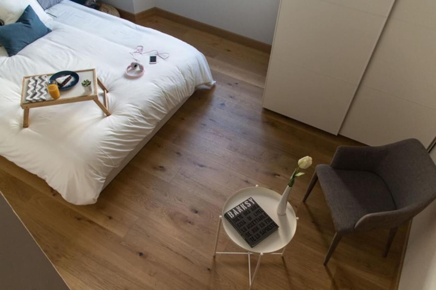 A bedroom with a bed, bedside table, chair, and a small table with a vase and a book.