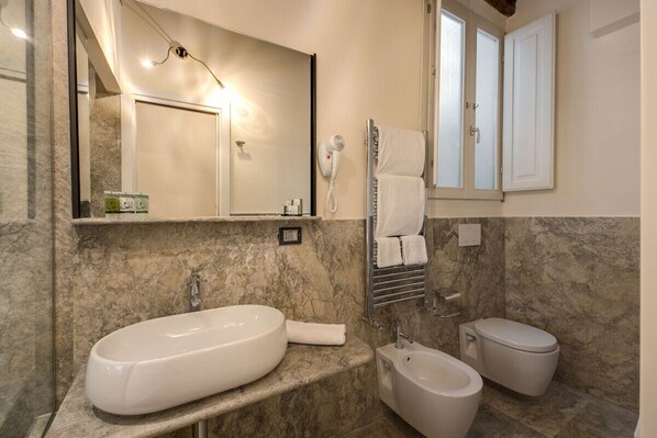 Un baño con un lavamanos ovalado grande, un bidé, un inodoro, un perchero para toallas y un espejo con iluminación.