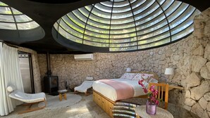 A bedroom with a stone wall, a bed, a TV, a chair, and a table with a vase of flowers. - Cabañas Caballieri (Paiguano)