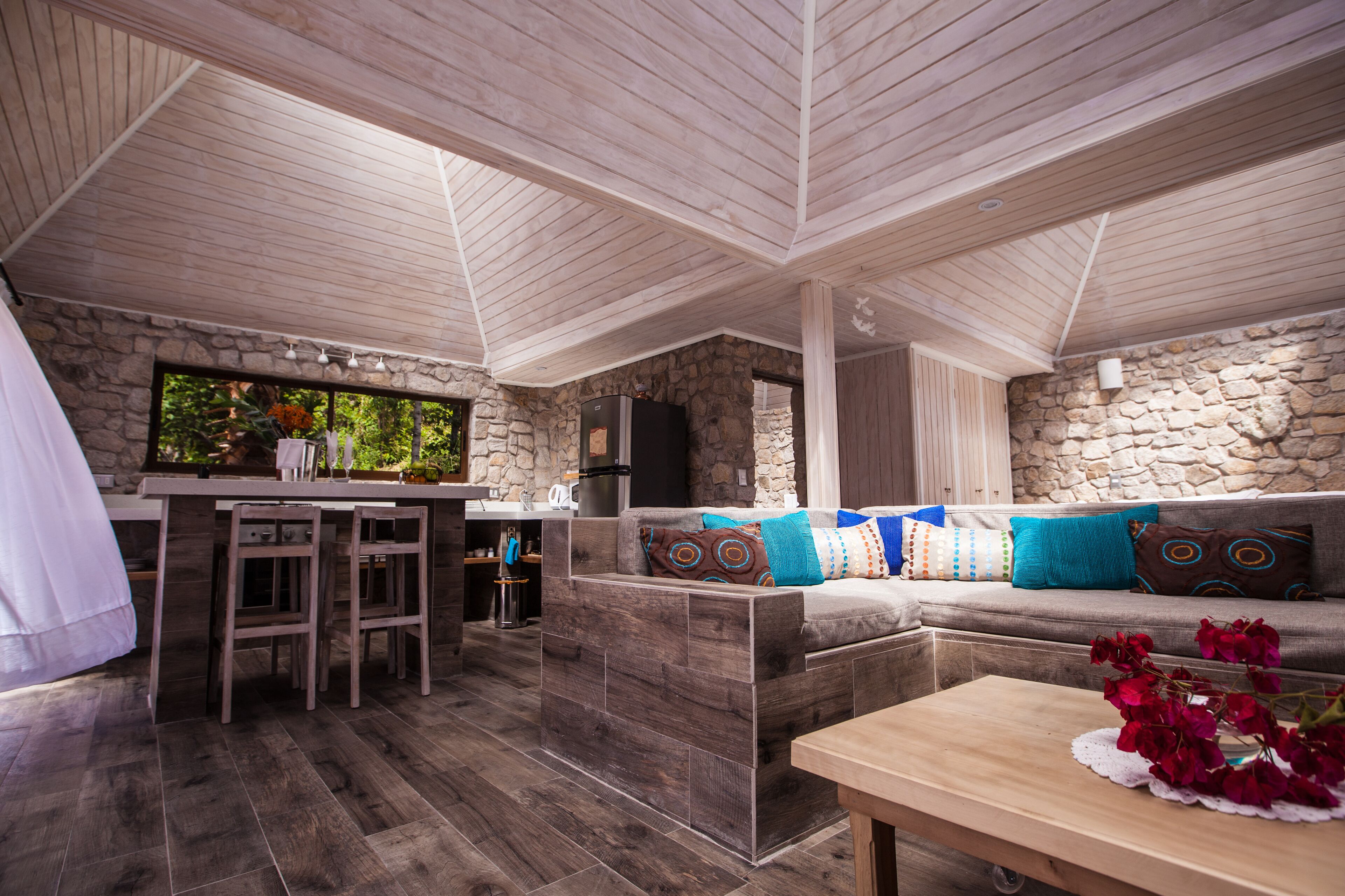 A cozy, open-plan living area with a stone wall, wooden ceiling, and a bar counter.