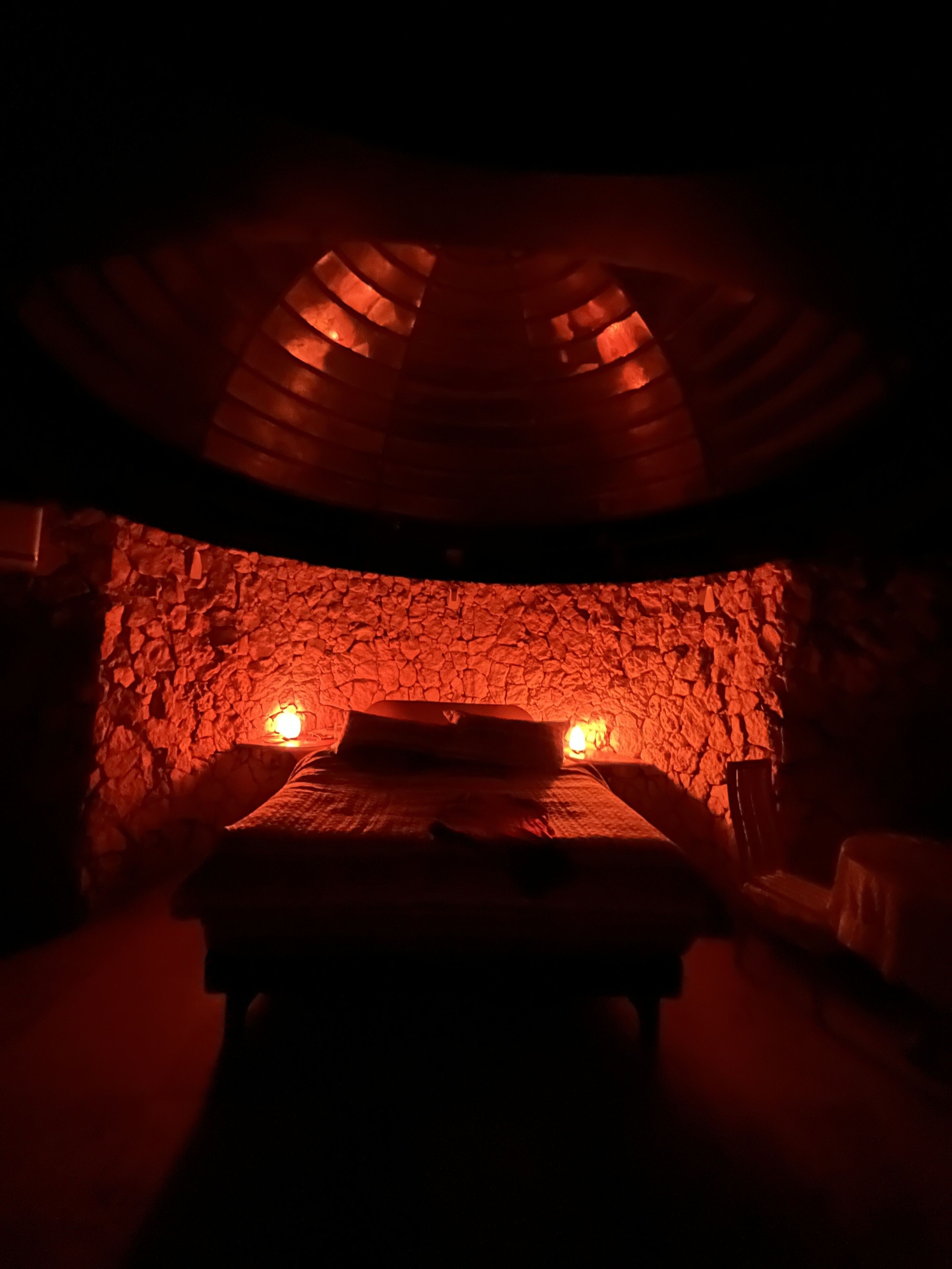 Una habitación tenuemente iluminada, con pared de piedra y una cama centrada en el espacio.