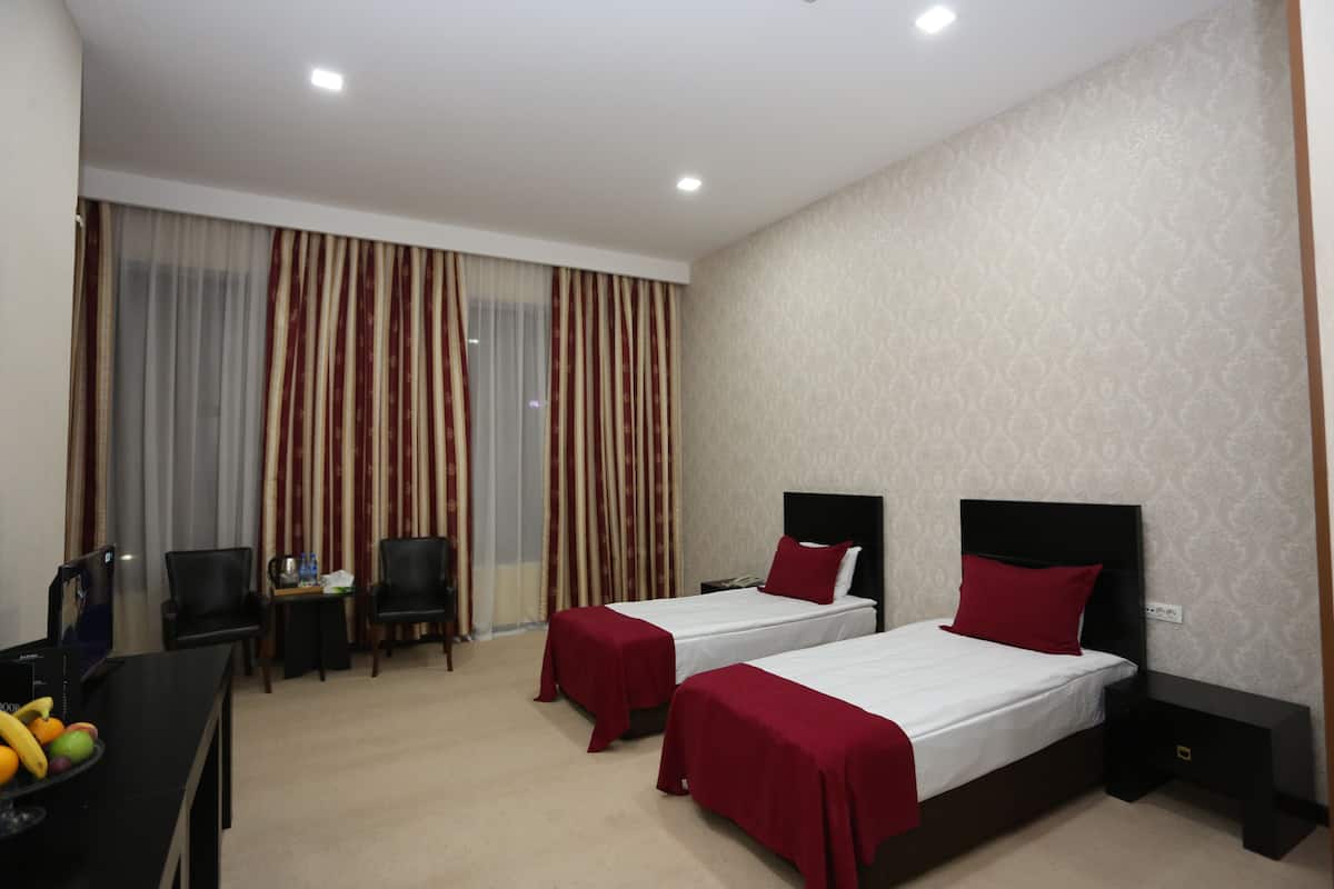 A hotel room with two single beds, a desk with a chair, a small table with a chair, and a fruit bowl.