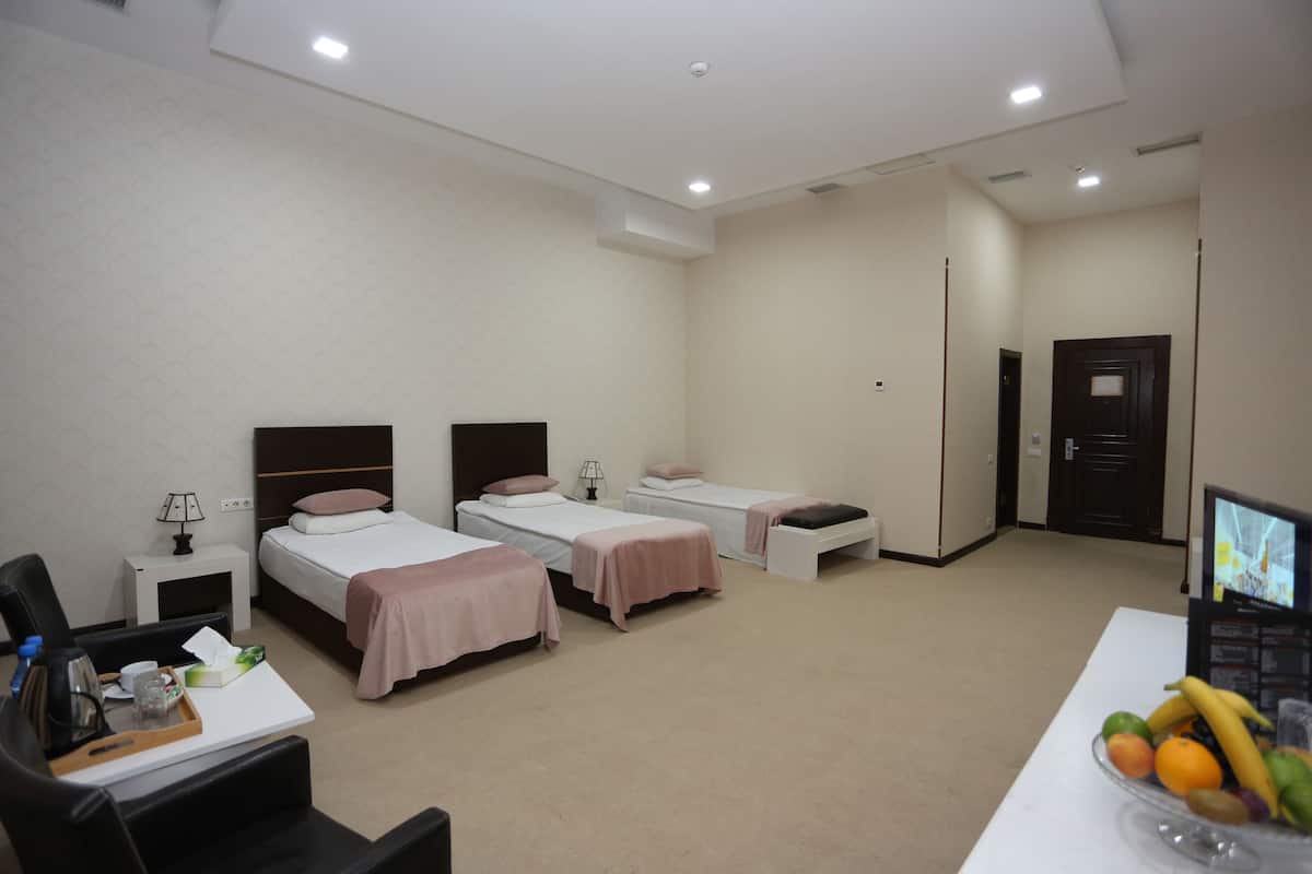A hotel room with three single beds, a desk with a computer, a chair, and a tray with toiletries.