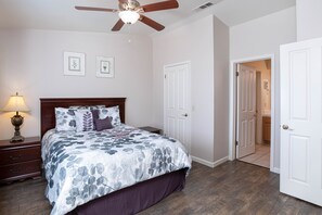 A bedroom with a bed, nightstand, lamp, ceiling fan, and two framed pictures on the wall.