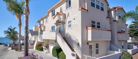 Um edifício residencial com vários andares, uma escadaria central, varandas e vista para o mar.