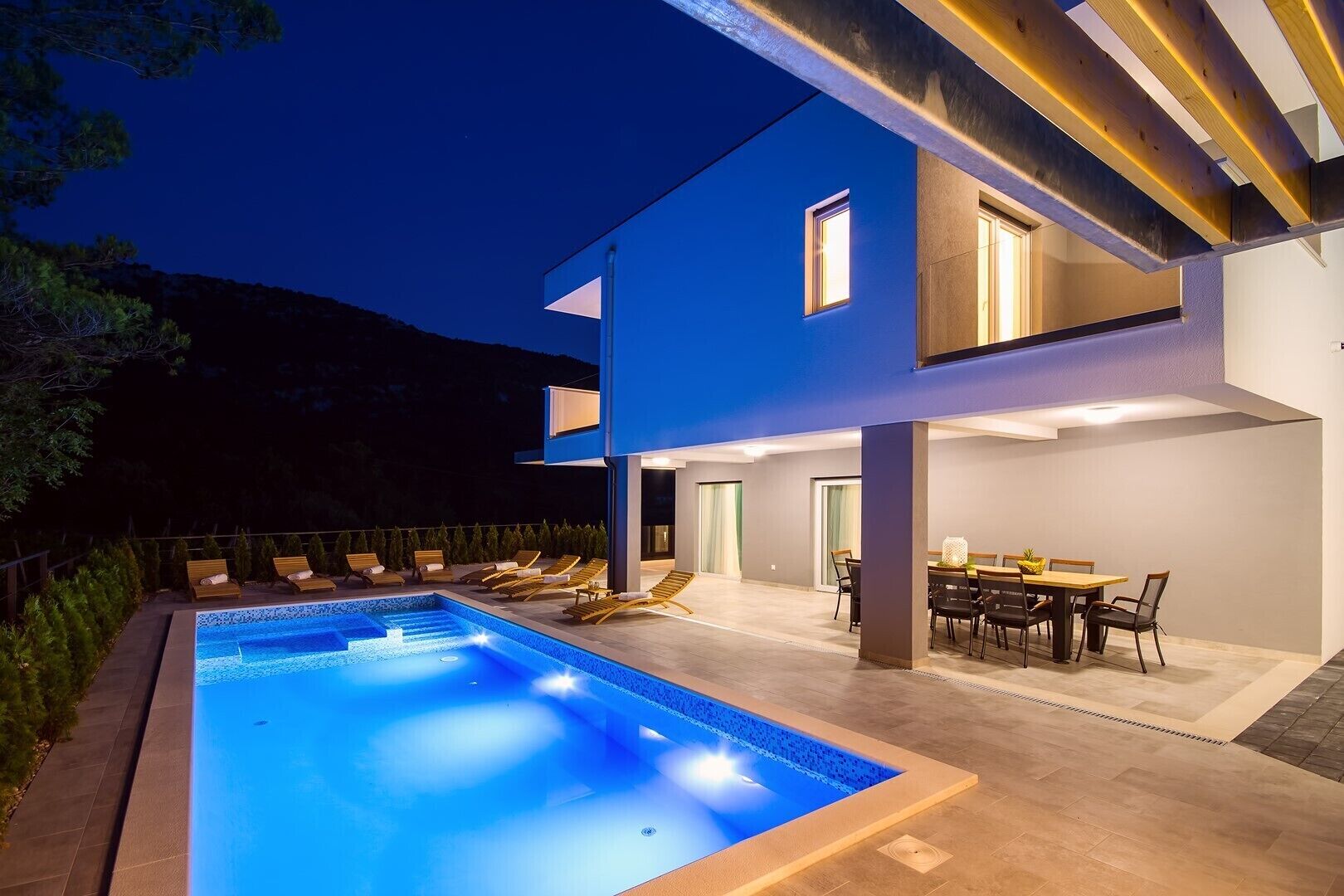 A modern two-story house with a swimming pool, outdoor seating, and a dining area.