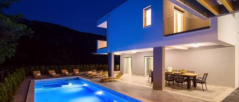 A modern two-story house with a swimming pool, outdoor seating, and a dining area.