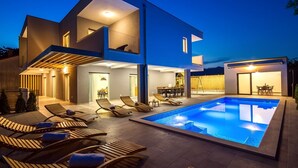 A modern two-story house with a swimming pool, outdoor seating, and a well-lit patio area. - Luxury Villa Tela with heated pool, attached whirlpool, sauna, darts, table tennis (Kucice)