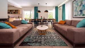 A modern living room with two sofas, a dining table, and a kitchen in the background. - Luxury Villa Tela with heated pool, attached whirlpool, sauna, darts, table tennis (Kucice)