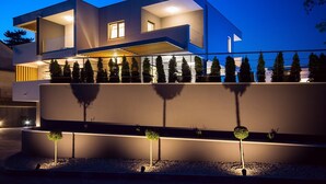 A modern two-story house with a flat roof, large windows, and a well-lit exterior. - Luxury Villa Tela with heated pool, attached whirlpool, sauna, darts, table tennis (Kucice)