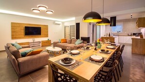 A modern living room with a sofa, a dining table set for six, and a kitchen in the background. - Luxury Villa Tela with heated pool, attached whirlpool, sauna, darts, table tennis (Kucice)