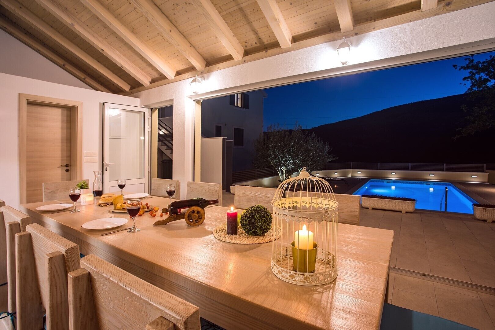 An outdoor dining area with a pool, wooden furniture, and a candle centerpiece.