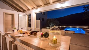 Un espace extérieur aménagé pour les repas, avec une piscine, des meubles en bois et un centre de table composé de bougies.