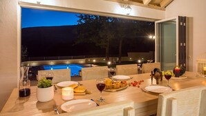 Un espace de restauration en plein air avec vue sur la piscine, doté de mobilier en bois et d’une table décorée de bougies.