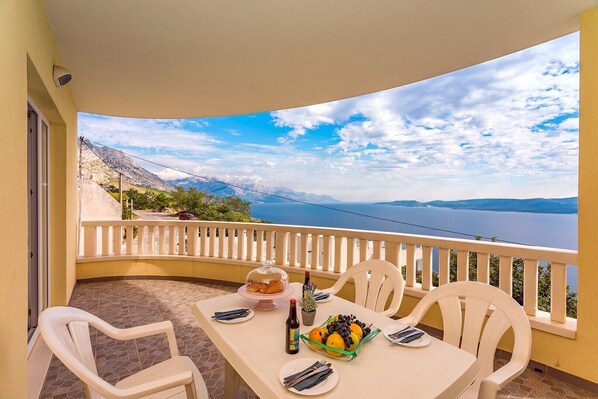 A balcony with a table set for two, overlooking a scenic view of a body of water and mountains.