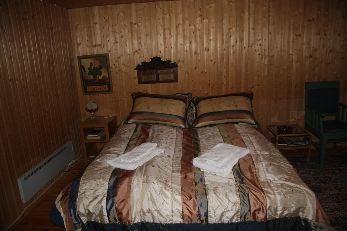 Quarto com painéis de madeira, uma cama, uma mesa de cabeceira, uma cadeira e um quadro na parede.