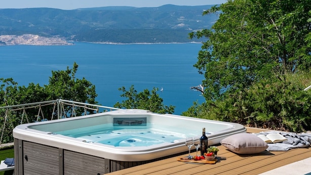 Un bain à remous avec une terrasse en bois et vue sur la mer.