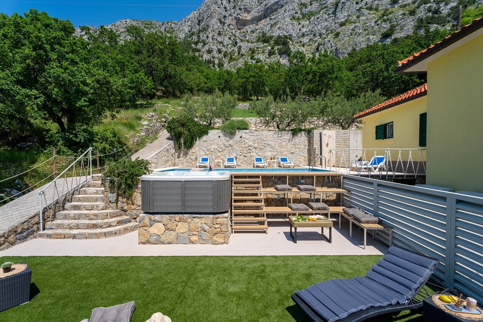 Un espace piscine doté d’un jacuzzi, de chaises longues et d’un escalier en pierre menant à un point de vue sur la montagne.