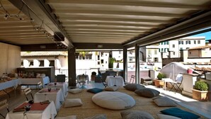 An outdoor dining area with tables and chairs, a covered seating area with cushions, and a view of the street. -  Residenze Argileto (Rome)